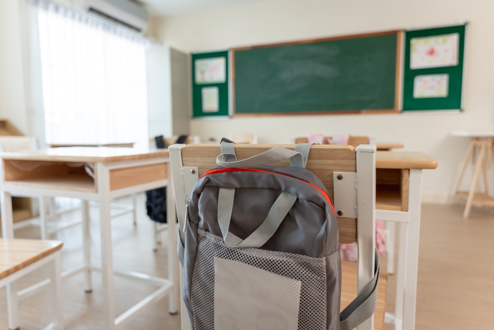 Backpack hanging on a chair in an empty classroom, representing the isolation students may feel when experiencing sexual harassment at school.


